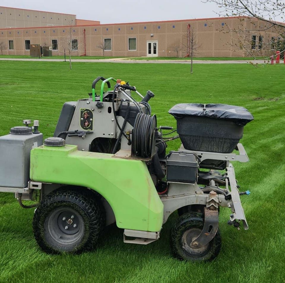 Commercial lawn care machine used for fertilization and weed control on a healthy green lawn in Central Minnesota, with a building in the background.